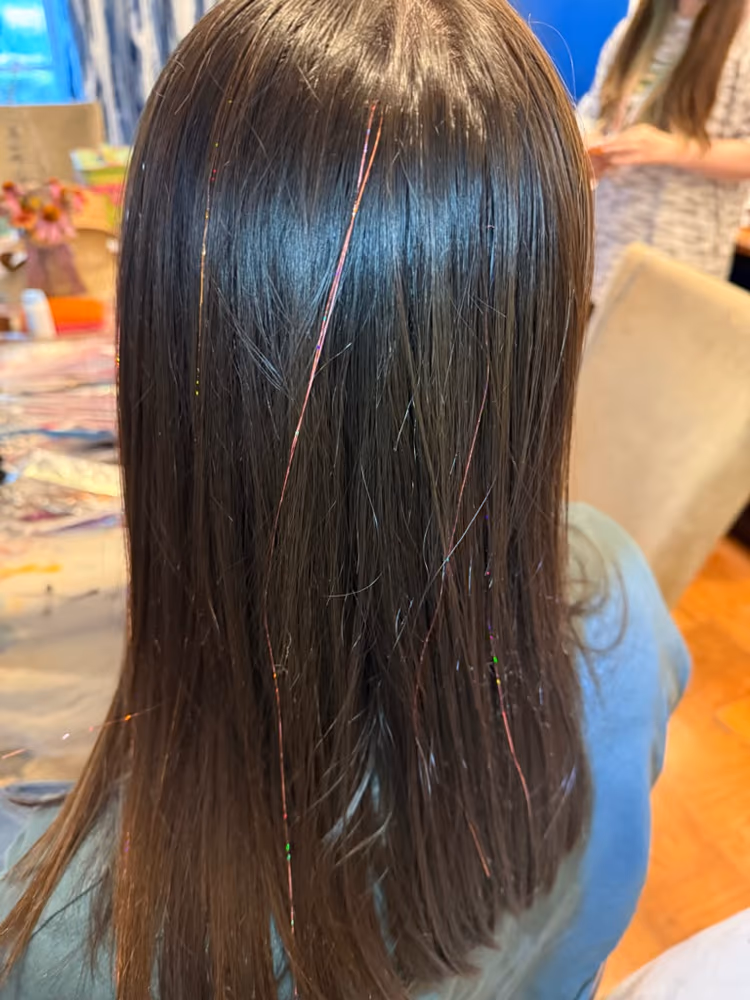 Long brown hair with iridescent fairy hair tinsel strands catching the light at a styling session