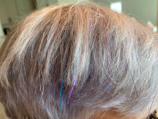 Close-up of blue, purple and pink fairy hair tinsel strands woven into light silver-blonde hair