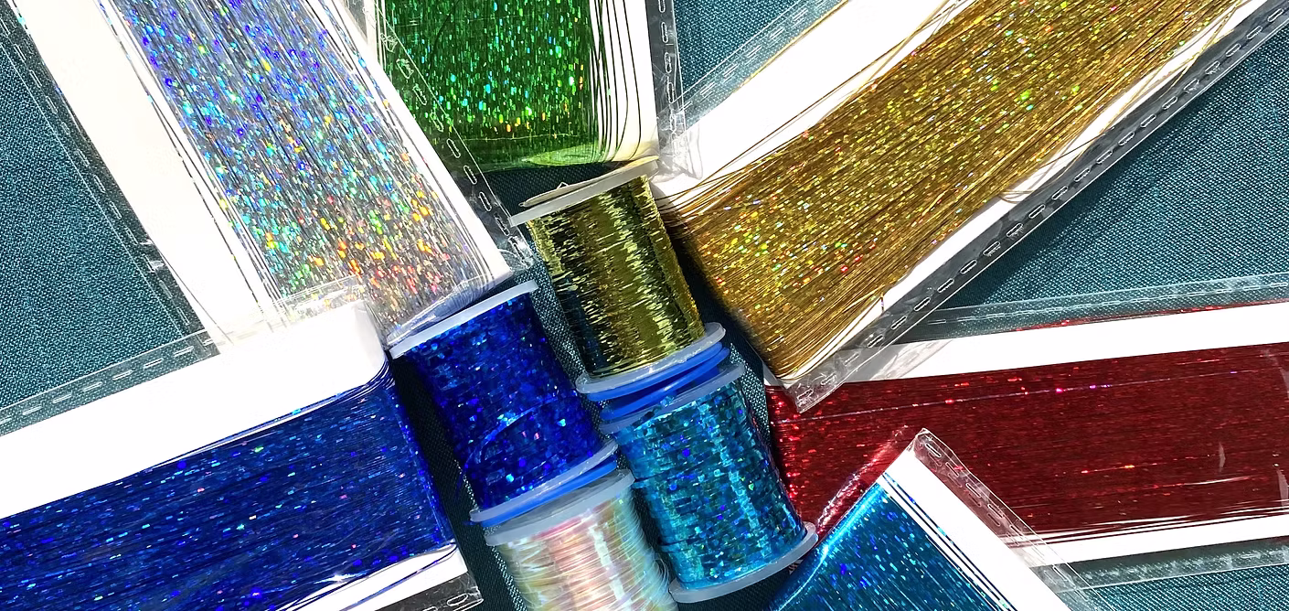 Spools of holographic tinsel in blue, green, and gold, ready to be tied in